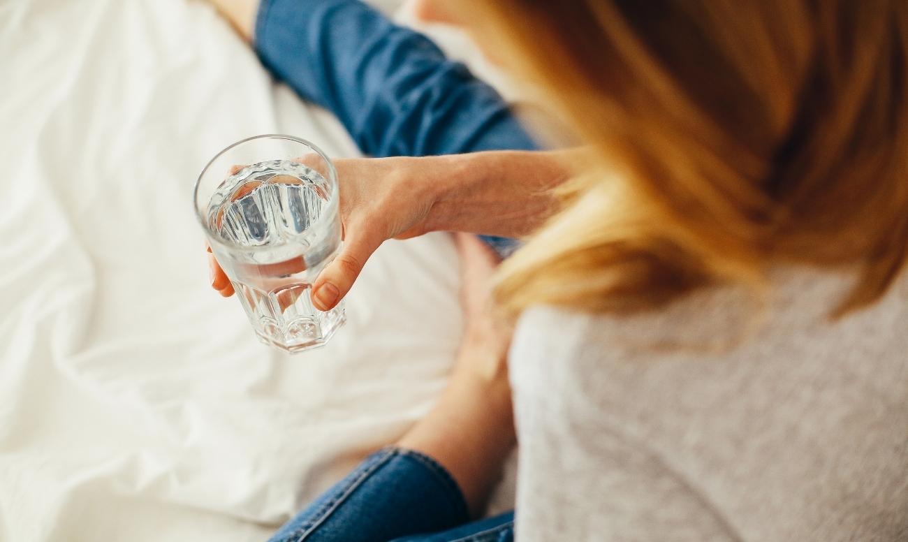 Ragazza bere un bicchiere d'acqua mentre la quantità di acqua che bisogna bere ogni giorno è pari a 2 lt.